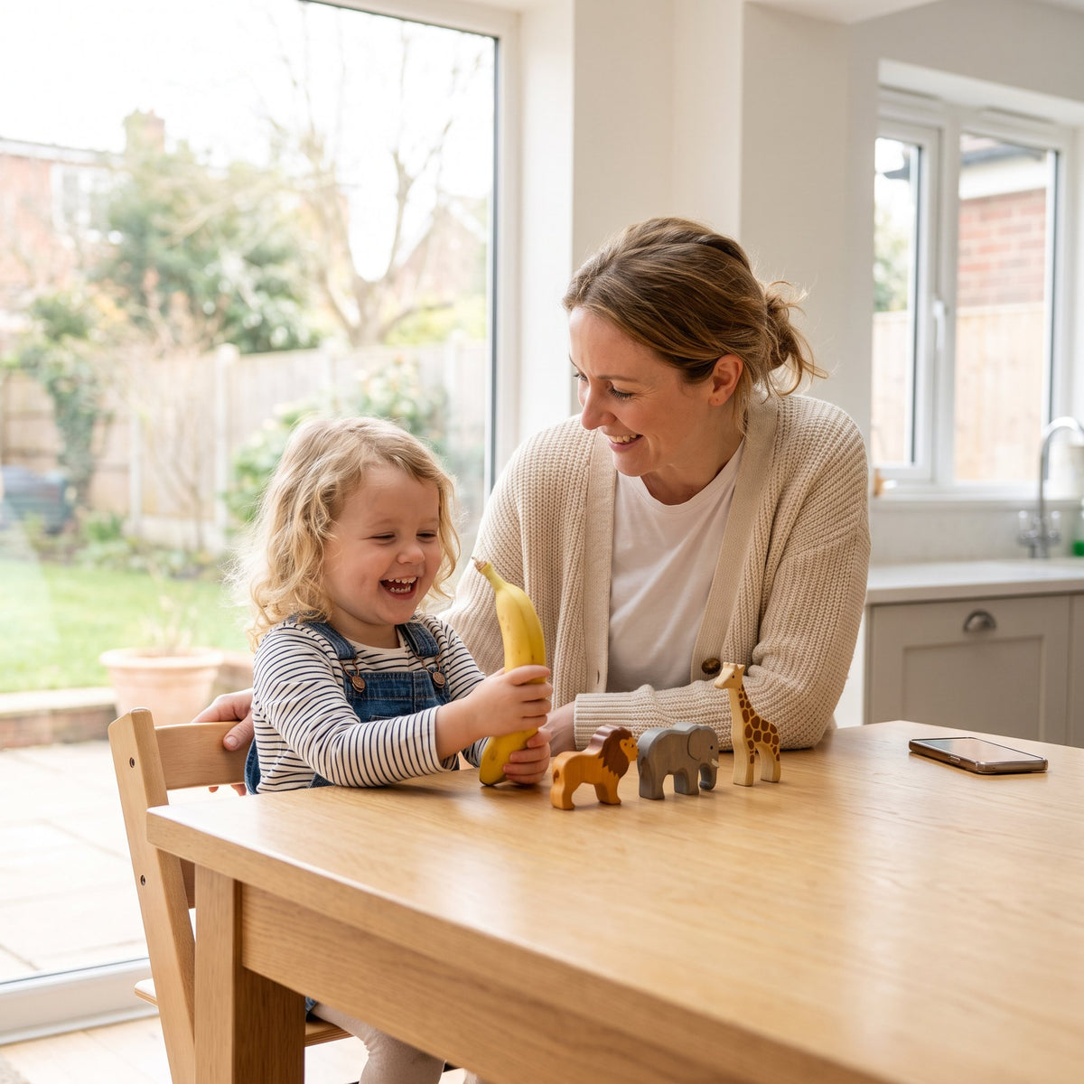 A parent and 3-year-old playing Odd One Out with household objects at the table
