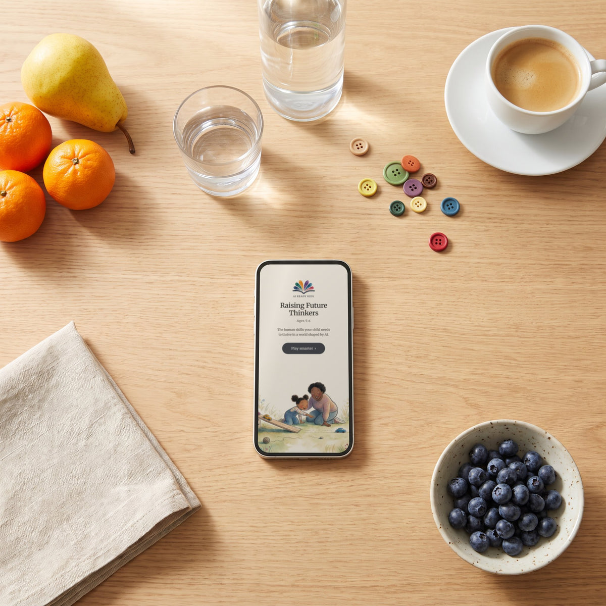 The Raising Future Thinkers ages 5–6 guide open on a phone on a breakfast table, beside glasses of water and coloured buttons
